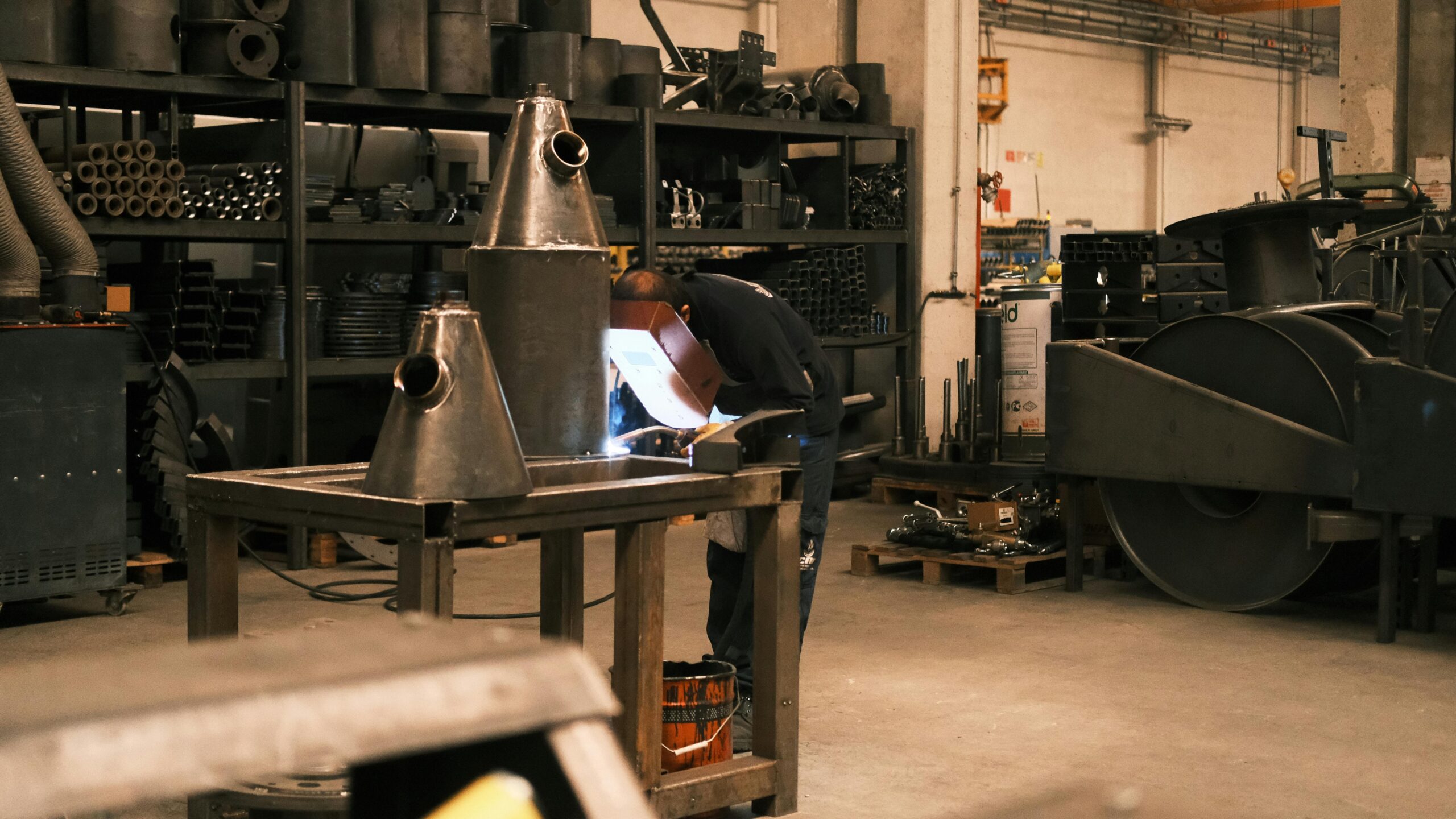 A skilled welder performs industrial welding in a metal workshop with equipment and safety gear.